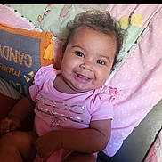 Cecelia joined the competition — help win amazing prizes! baby, blanket, candid, child, cozy, curly_hair, cute, face, happy, indoor, infant, person, pillow, pink_clothing, portrait, sitting, skin, smiling, soft_toys, young