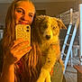 woman, puppy, dog, selfie, indoor, long_hair, smile, bunk_bed, bedroom, phone, hand, casual_clothing, furniture, carpet, warm_lighting, young_adult, holding, pet, cute, portrait