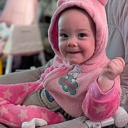 Eloise is registered to the contest to win money with this photo: baby, child, pink_clothing, onesie, hood, bear_ears, smile, face, infant, sitting, baby_chair, indoor, cute, happy, fist, soft_texture, cozy, apparel, young_child, plush