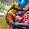 child, toddler, car_seat, plush_toys, pikachu, blue_mouse, car_interior, seatbelt, smiling, red_clothing, sunroof, window, daylight, safety_harness, toy, cute, happy, travel, road_trip, car