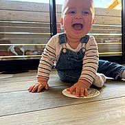 Théo a rejoint le concours — aidez-le/la à gagner de superbes lots ! baby, child, smiling, happy, denim_overalls, striped_shirt, floor, wooden_floor, indoor, natural_light, window, glass_door, playful, cute, young_child, person, hand, face, sitting, card