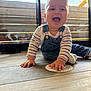 baby, child, smiling, happy, denim_overalls, striped_shirt, floor, wooden_floor, indoor, natural_light, window, glass_door, playful, cute, young_child, person, hand, face, sitting, card