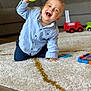 toddler, child, indoor, carpet, toy, tennis_ball, smiling, happy, blue_shirt, playing, living_room, couch, fire_truck_toy, floor, young_child, casual_clothing, cheerful, kneeling, home, fun