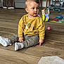 Théo participe au concours pour gagner de l'argent avec cette photo : toddler, child, indoor, floor, wooden_floor, sweatshirt, pants, white_shoes, toy, living_room, couch, curious, pointing, seated, person, home, casual_clothing, young_child, playtime, expression