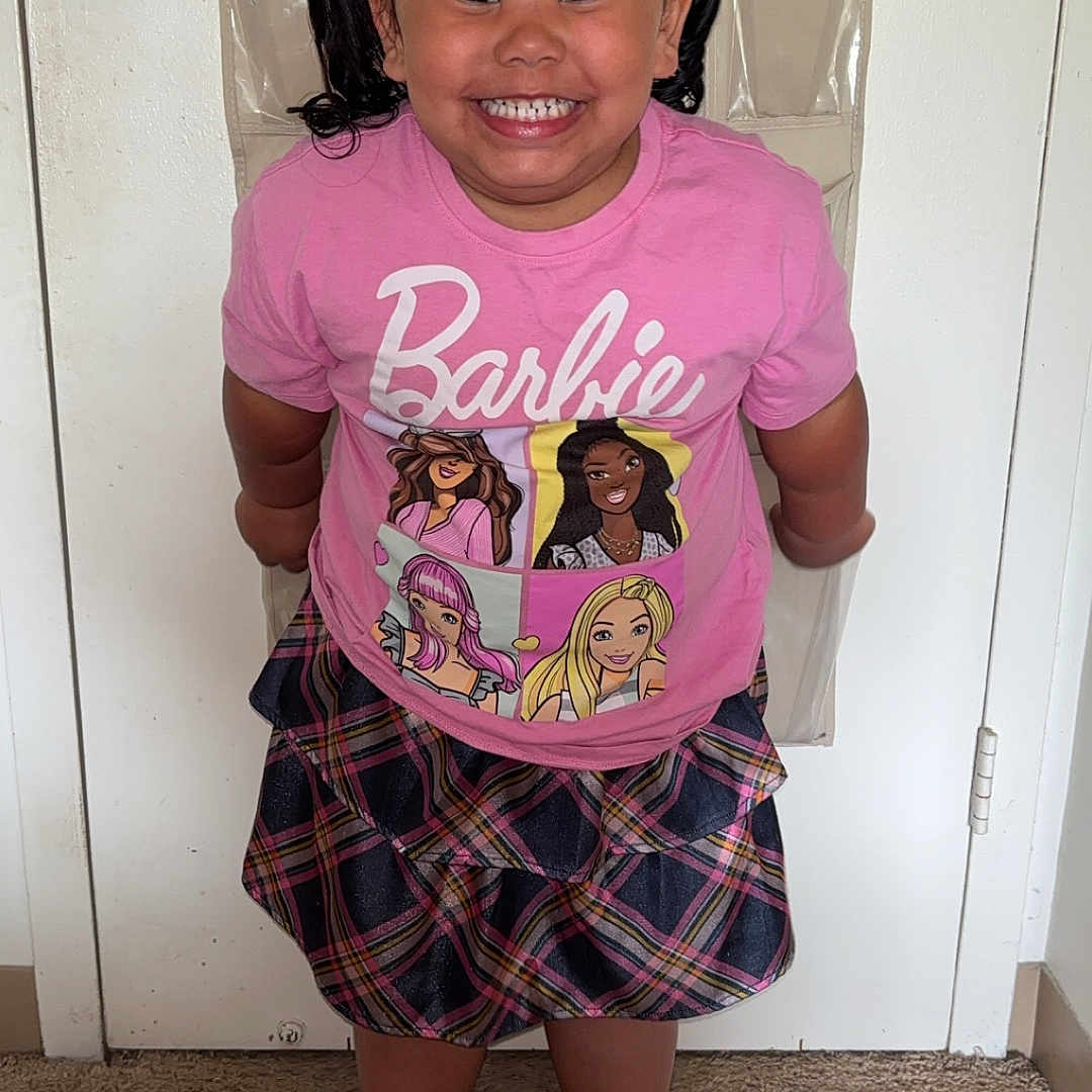Elaina is registered to the contest to win money with this photo: barbie, barefoot, carpet, child, clothing, door, girl, hair_bows, happy, indoors, organizer, person, pigtails, pink_shirt, plaid_skirt, portrait, room, smiling, standing, wall