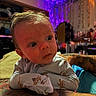 Anakin is registered to the contest to win money with this photo: baby, infant, tattoo, arm, indoor, curious, wide_eyes, hair, clothing, pajamas, colorful_lighting, purple_light, orange_light, cozy, resting, portrait, face, child, person, blurred_background