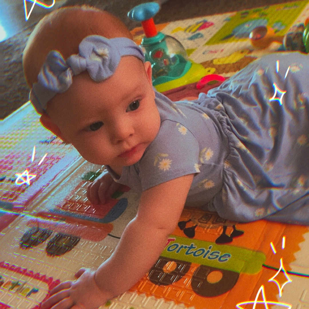 Luna is registered to the contest to win money with this photo: baby, child, play_mat, crawling, headband, dress, indoor, cute, colorful, toy, animal, floor, exploration, star_doodles, infant, childhood, patterned_clothing, playtime, curious, soft_lighting