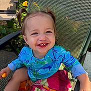 Lailah joined the competition — help win amazing prizes! child, toddler, smiling, happy, portrait, outdoor, patio, chair, pigtails, blue_shirt, colorful_clothing, fruit, snack, food, garden, plants, flowers, sunlight, seated, closeup