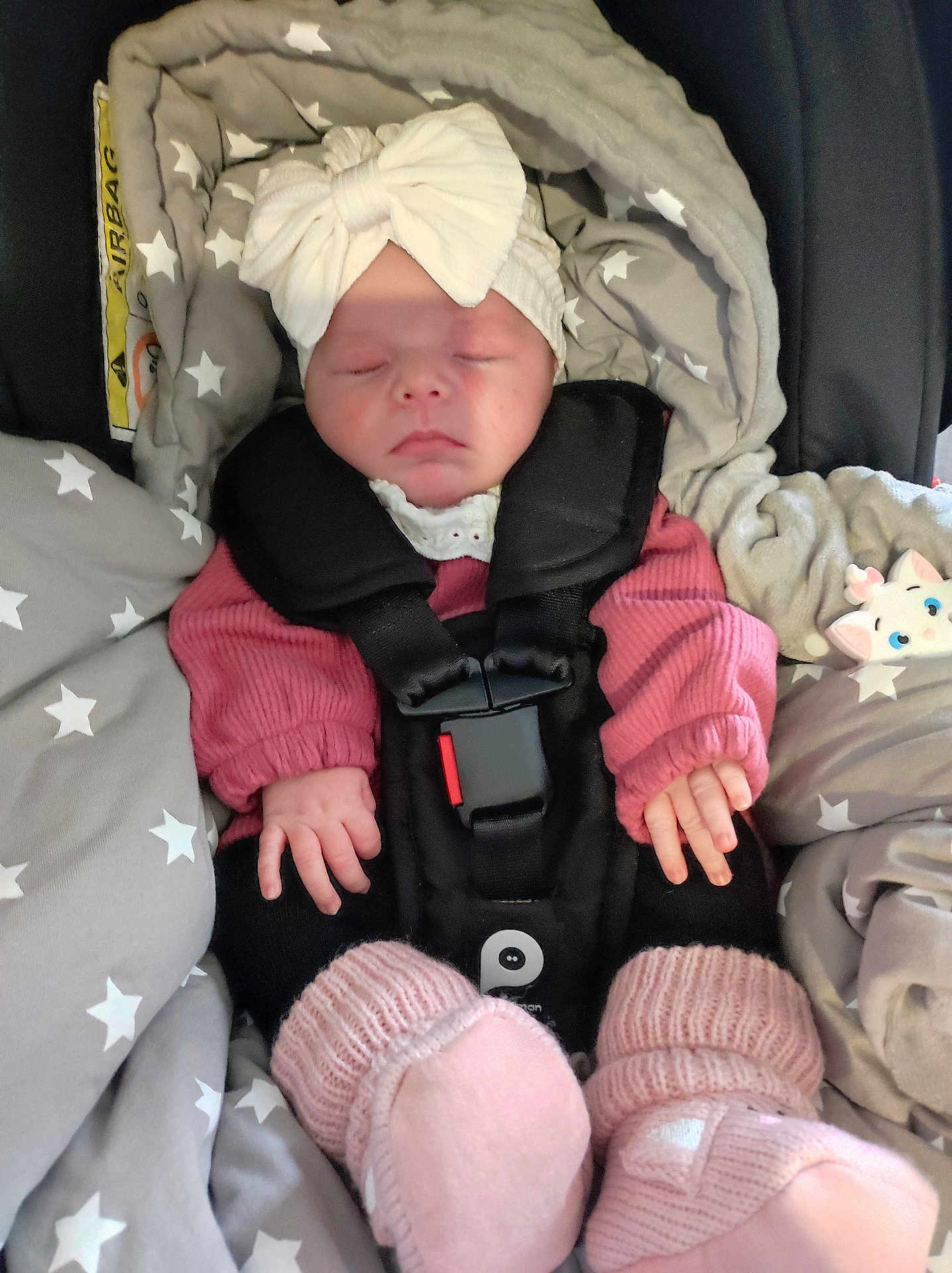 Romy participe au concours pour gagner de l'argent avec cette photo : baby, sleeping, car_seat, blanket, bow, headband, pink_booties, star_pattern, cozy, child, infant, clothing, soft_toy, resting, indoors, cute, hands, face, straps, comfort