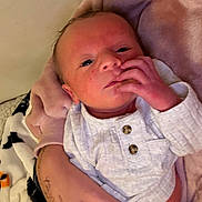 Daniel is registered to the contest to win money with this photo: baby, blanket, buttons, closeup, clothing, cozy, cute, eyes, face, hand, holding, human, indoor, infant, newborn, person, portrait, skin, soft, white_outfit
