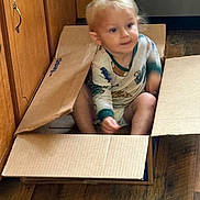 Samuel joined the competition — help win amazing prizes! toddler, child, cardboard_box, pajamas, indoor, wooden_floor, kitchen, cabinet, floor, young_child, sitting, playful, blurry, cute, person, home, casual, relaxed, small_child, light