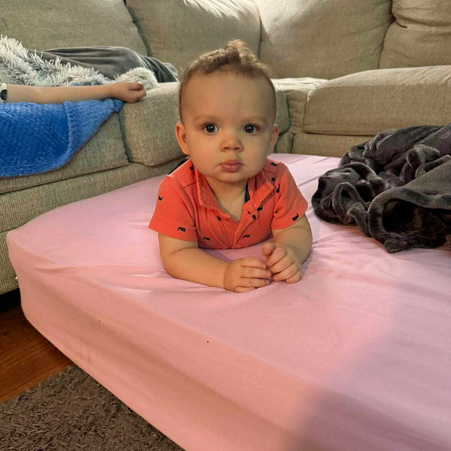 Cyndrik is registered to the contest to win money with this photo: baby, blanket, carpet, casual_clothing, child, couch, curly_hair, floor, furniture, home, indoor, lamp, living_room, mattress, orange_shirt, person, portrait, relaxed, toddler, young_child