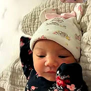 Leilani is registered to the contest to win money with this photo: baby, infant, child, portrait, floral_outfit, knitted_hat, hat, sleeping, awake, face, smiling, bed, blanket, indoors, baby_clothing, floral_pattern, video_call, adult, photobomb, cozy