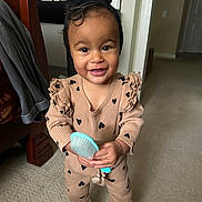 Farrah joined the competition — help win amazing prizes! toddler, child, smiling, indoor, carpet, hairbrush, black_headband, beige_outfit, hearts_pattern, barefoot, bed, door, furniture, person, happy, cute, young_child, standing, home, portrait