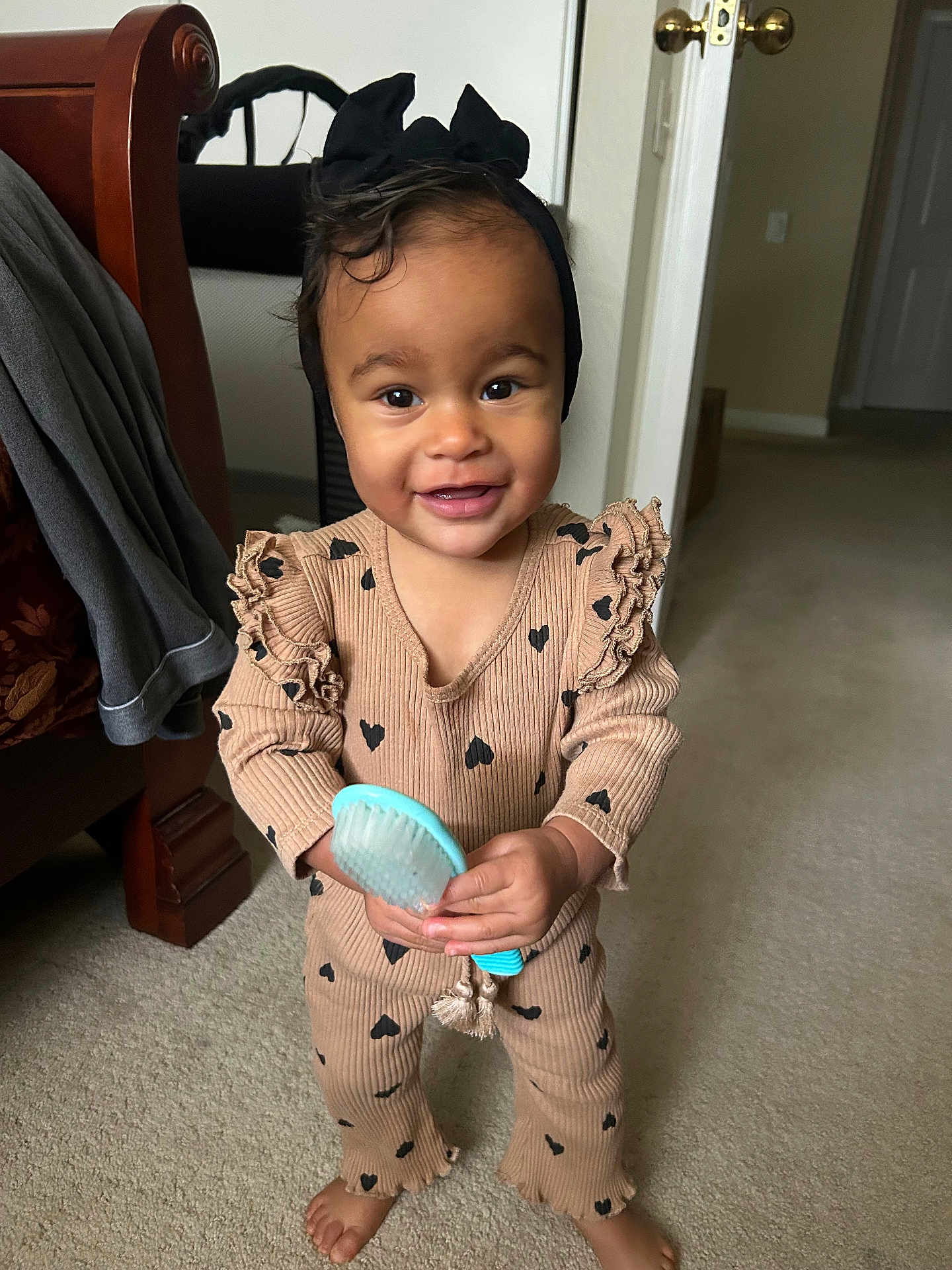 Farrah joined the competition — help win amazing prizes! toddler, child, smiling, indoor, carpet, hairbrush, black_headband, beige_outfit, hearts_pattern, barefoot, bed, door, furniture, person, happy, cute, young_child, standing, home, portrait