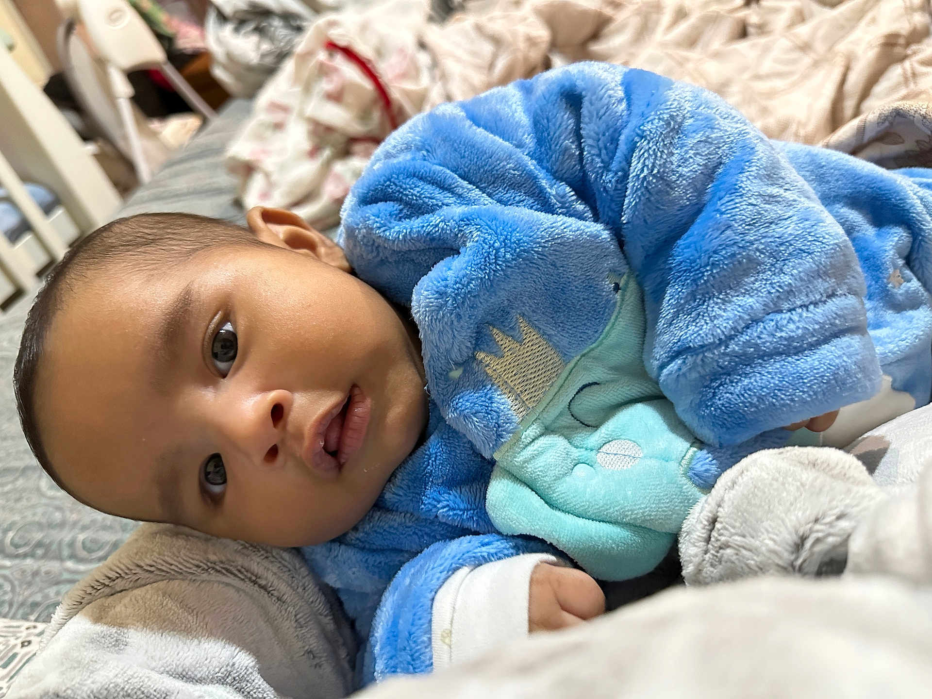 Aarin is registered to the contest to win money with this photo: baby, infant, blue_onesie, blanket, soft_texture, face, eyes, hand, mouth, indoor, bed, cushion, cute, child, newborn, warm, cozy, sleepwear, portrait, person