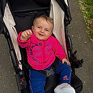 Jihane a rejoint le concours — aidez-le/la à gagner de superbes lots ! baby, child, stroller, outdoor, pavement, pink_jacket, blue_pants, white_shoes, happy, smiling, person, infant, casual_clothing, grass, sidewalk, cute, young_child, seatbelt, nature, playful