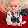 baby, child, infant, denim_overalls, white_shirt, tattoo, hand, red_blanket, couch, cushion, indoor, person, sitting, cute, blue_eyes, sock, holding_foot, expression, support, soft_furniture