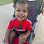 toddler, child, stroller, smiling, red_shirt, adidas, outdoor, sidewalk, grass, happy, person, footwear, black_shoes, mickey_mouse_pattern, sunny, daytime, cute, young_child, casual_clothing, park