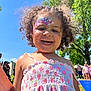 child, girl, face_paint, curly_hair, smiling, outdoor, sunny, blue_sky, dress, people, trees, grass, summer, happy, portrait, daylight, park, event, cute, joyful