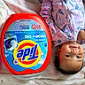 Ada is registered to the contest to win money with this photo: baby, infant, smile, face, hand, bracelet, clothing, floral_pattern, blanket, detergent, laundry_pods, tide, container, soft, indoors, cute, lying_down, domestic, child, portrait