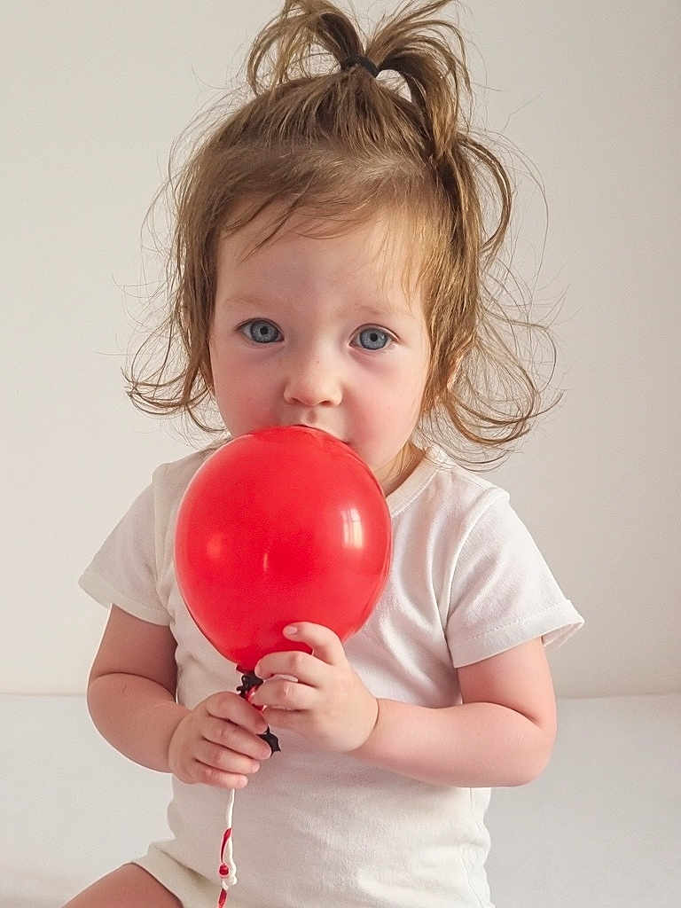 Selena joined the competition — help win amazing prizes! toddler, child, balloon, red_balloon, white_shirt, light_background, portrait, cute, innocent, blue_eyes, sitting, hands, hair_tied, indoor, young_child, baby, face, expression, holding, playful