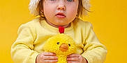 Selena is registered to the contest to win money with this photo: toddler, child, yellow, plush_toy, chicken_hat, cute, soft_texture, indoor, portrait, baby, costume, sitting, orange, yellow_background, toy, funny_hat, young_child, clothing, face, hands