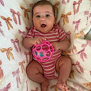 Avilyn is registered to the contest to win money with this photo: baby, blanket, bows, child, cute, expression, face, happy, holding, indoor, infant, person, pink_onesie, playful, small_feet, small_hands, smiling, soft_texture, striped_clothing, toy