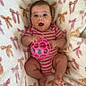 baby, infant, toy, pink_onesie, striped_clothing, blanket, bows, soft_texture, child, cute, playful, indoor, person, smiling, happy, small_hands, small_feet, face, expression, holding