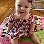 baby, infant, smiling, sitting, headband, dress, patterned_clothing, blanket, wooden_floor, indoors, child, cute, happy, face, person, toy, floor, colorful, home, portrait