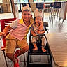 child, toddler, smiling, crown, restaurant, high_chair, red_crocs, shorts, striped_shirt, table, chair, floor, window, daylight, happy, family, indoor, person, cute, playful
