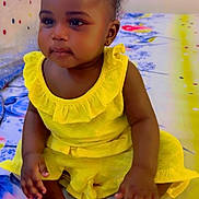 Afrah is registered to the contest to win money with this photo: toddler, child, yellow_dress, sitting, indoor, bedspread, colorful, feet, hands, curly_hair, portrait, cute, young_child, person, baby, smiling, happy, skin, room, furniture