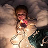 Damon is registered to the contest to win money with this photo: toddler, child, lights, string_lights, cloud, soft_texture, curious, glowing, indoors, warm_light, cozy, casual_clothing, expression, portrait, candid, laying_down, young_child, hands, nighttime, imaginative
