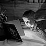 Damon joined the competition — help win amazing prizes! child, toddler, reading, book, christmas, holiday, present, gift, black_and_white, indoors, curious, face, portrait, light, shadow, blanket, floor, focus, cozy, winter