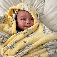Lorenzo is registered to the contest to win money with this photo: baby, bed, blanket, cartoon_print, child, comfort, cozy, cute, face, happy, human, indoors, infant, portrait, smile, soft, warm, white_background, wrapped, yellow
