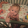 baby, child, infant, crib, crib_rail, floral_bedding, bedroom, indoors, portrait, face, smiling, curious, sitting, standing, hand, striped_shirt, toy, clothing, wooden_furniture, home