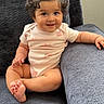baby, child, toddler, sitting, smiling, portrait, curly_hair, topknot, pink_outfit, onesie, barefoot, couch, indoor, home, furniture, happy, infant, arms, legs, photography