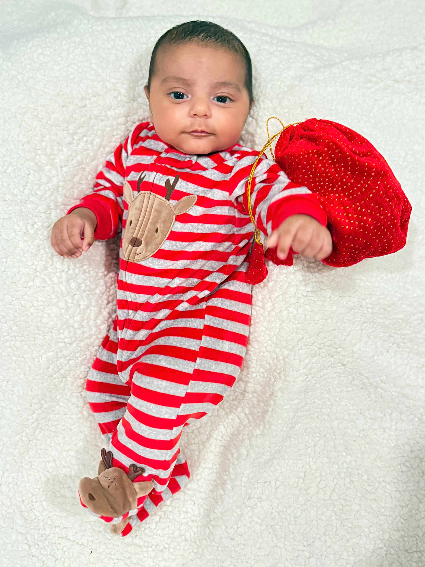 Aviraj is registered to the contest to win money with this photo: baby, infant, pajamas, striped_clothing, reindeer_design, red_clothing, gray_stripes, blanket, white_blanket, plush_texture, lying_down, hand, face, eyes, cute, child, holiday_theme, velvet_pouch, red_pouch, soft_lighting