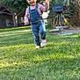 toddler, child, grass, outdoor, smiling, happy, denim_overalls, pink_sneakers, waving, sunlight, backyard, trees, barbecue_grill, person, nature, daylight, playful, cute, casual_clothing, young_child