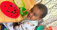 Rhett is registered to the contest to win money with this photo: blueberries, booster_seat, bowl, chair, child, curtains, dinosaur_pattern, face, food, happy, home, indoor, meal, pajamas, plate, smile, spoon, table, toddler, wooden_table