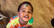 Rhett joined the competition — help win amazing prizes! child, smiling, tie_dye_shirt, sticker, floor, wooden_floor, indoors, person, happy, looking_up, curly_hair, barefoot, home, casual, playful, face, cute, young, boy, portrait