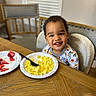 toddler, child, smiling, breakfast, scrambled_eggs, strawberries, paper_plate, fork, pajamas, table, wooden_table, chair, high_chair, indoor, happy, food, meal, cute, face, person