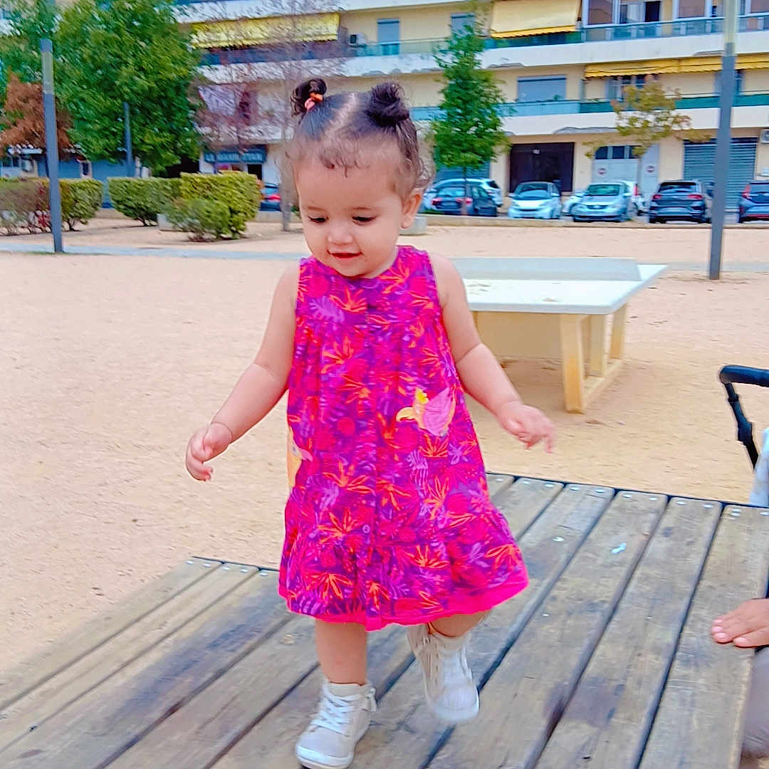 Abidi Amira participe au concours pour gagner de l'argent avec cette photo : buildings, cars, child, daylight, dress, hair_buns, happy, outdoor, park, person, pink, playground, shoes, sidewalk, sneakers, toddler, trees, urban, walking, wooden_platform