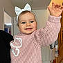 baby, child, smiling, blue_eyes, white_bow, pink_sweater, knitted_clothing, indoor, home, stairs, radiator, person, happy, cute, waving_hand, face, headband, cozy, toddler, portrait