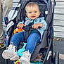 toddler, stroller, child, boots, jeans, denim_jacket, toy_keys, outdoor, person, blue_eyes, smiling, hand, fence, wheel, pavement, jacket, clothing, face, happy, baby_toy