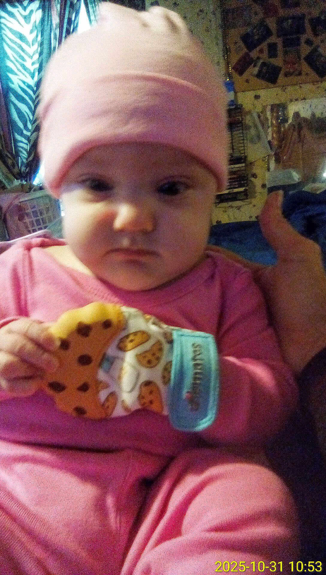 Nova joined the competition — help win amazing prizes! baby, child, pink_clothing, hat, teething_mitten, cookie_pattern, indoor, furniture, curtain, face, hand, person, clothing, expression, seated, room, background, household_items, portrait, serious