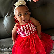 Laniya is registered to the contest to win money with this photo: toddler, child, red_dress, headband, flower, striped_clothing, sitting, leather_couch, curious_expression, indoor, person, fashion, cute, young_child, casual, portrait, face, eyes, hair, couch