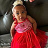 toddler, child, red_dress, headband, flower, striped_clothing, sitting, leather_couch, curious_expression, indoor, person, fashion, cute, young_child, casual, portrait, face, eyes, hair, couch