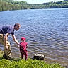 Brytton is registered to the contest to win money with this photo: lake, water, adult, child, grass, nature, forest, outdoor, person, toddler, red_clothing, blue_shirt, tree, sunlight, shore, summer, helping, candid, scenic, recreation