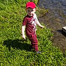 Brytton is registered to the contest to win money with this photo: child, boy, red_cap, red_clothing, grass, river, water, outdoor, nature, greenery, shadow, sunlight, standing, curious, casual_clothing, daylight, young, person, scenic, portrait